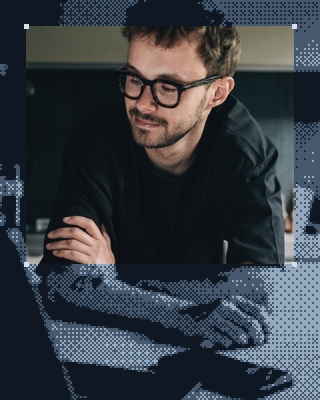 Un homme à lunettes, les bras croisés à son bureau.