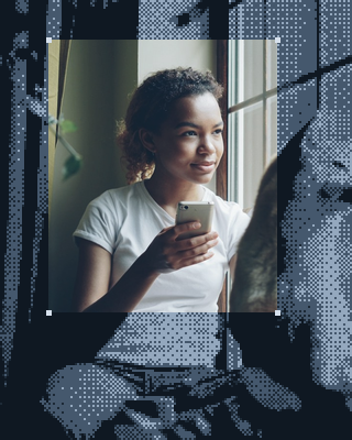 Une jeune femme regarde par la fenêtre, son téléphone à la main.